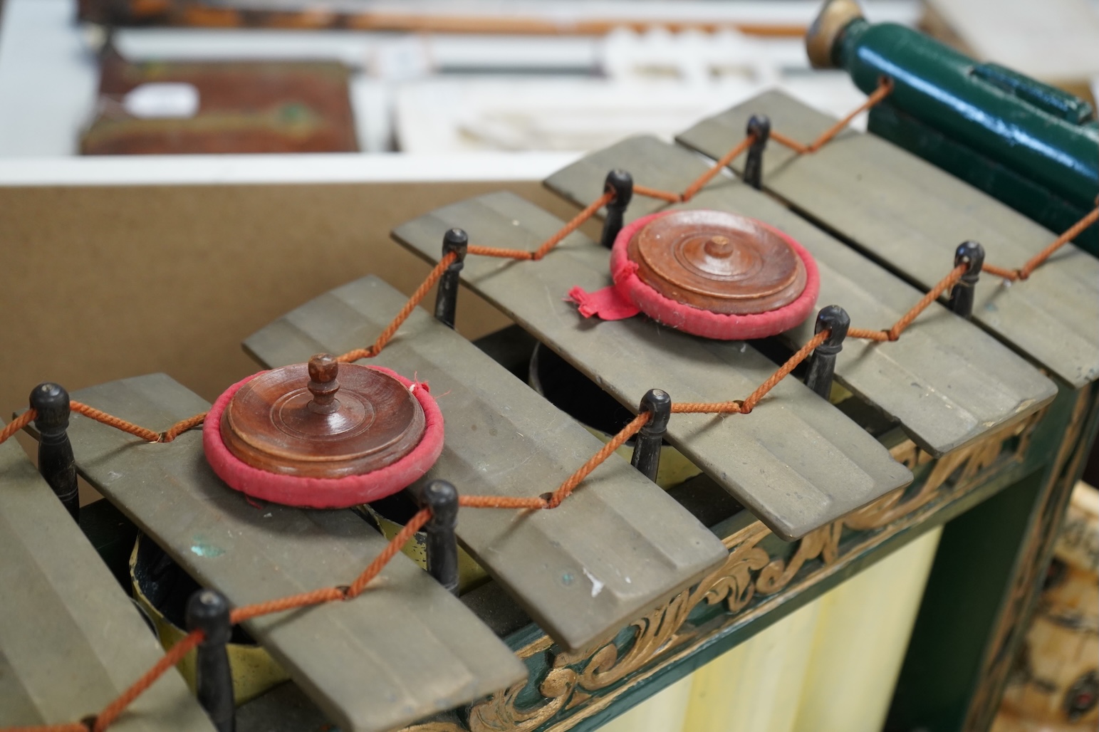 A green and gold painted wooden Javanese Gamelan Slenthem musical instrument, 61cm wide, 46cm high, together with two hammers